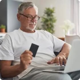 Hombre sosteniendo una tarjeta de crédito mientras escribe en su laptop